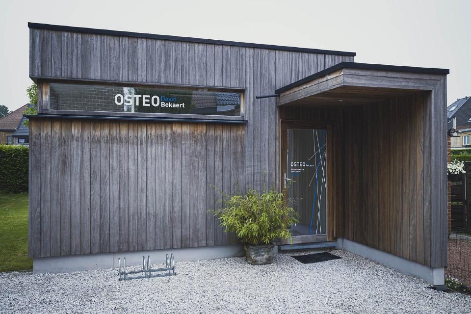 Buitenkant van de praktijk met houten gevel en het bord OsteoBekaert